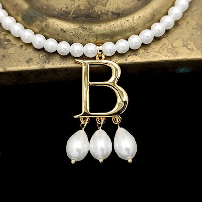 Close-up photo of Anne Boleyn's necklace showing the letter B with the three medium-sized pearl pendants resting on the base of a brass candlestick.