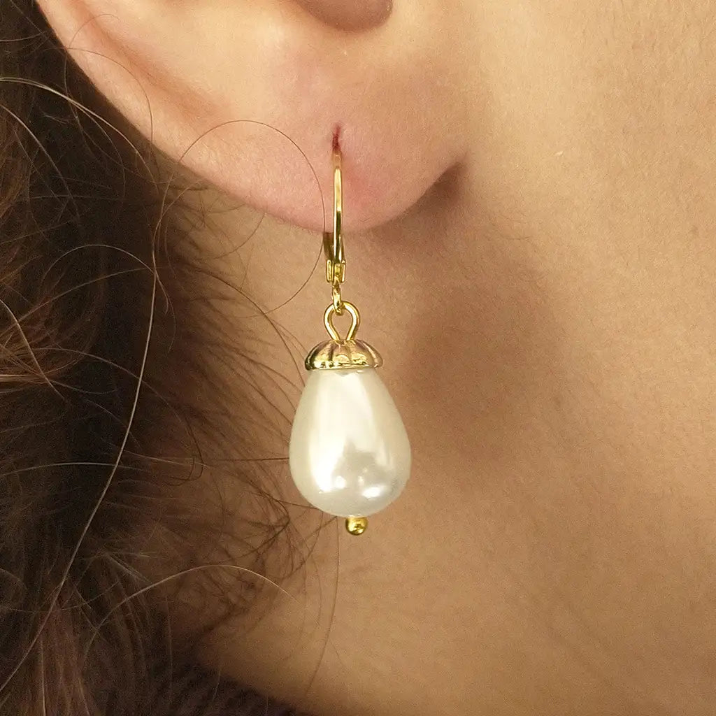 Close up image of the Lucrezia earrings with 10x14 mm. shell pearls with opalescent finish and gold-plated caps holding the pearls up to the clasp on a ear model.