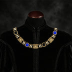 Frontal view of Ambrossio chain of foffice in brass finish with two strand of pearls and bLue and black cabochons on a black doublet mannequin