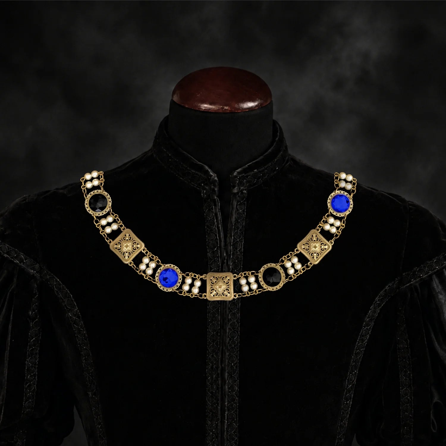 Frontal view of Ambrossio chain of foffice in brass finish with two strand of pearls and bLue and black cabochons on a black doublet mannequin