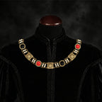 Frontal view of Ambrossio chain of foffice in brass finish with two strand of pearls between connectors and settings with Red and Black cabochons on a black doublet mannequin