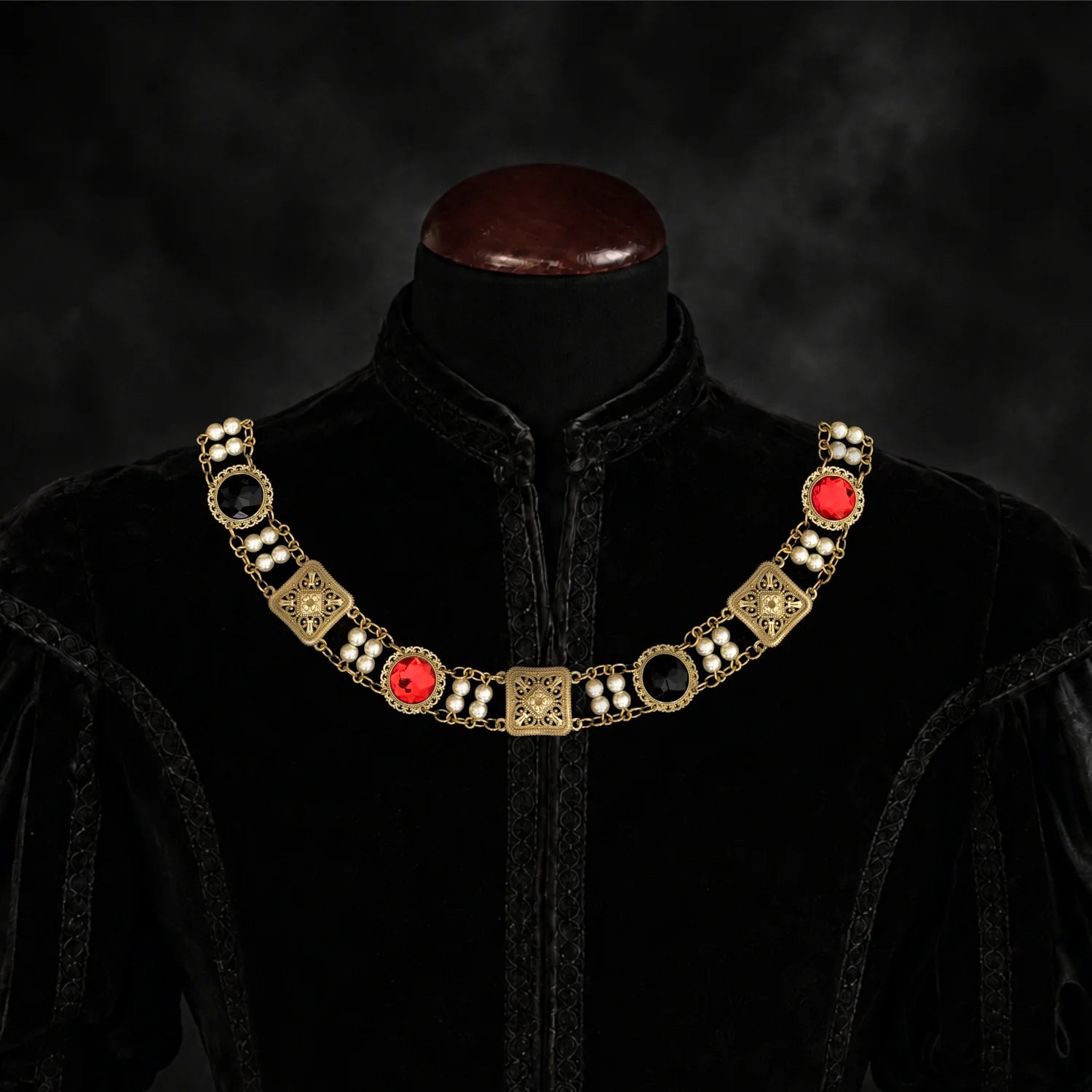 Frontal view of Ambrossio chain of foffice in brass finish with two strand of pearls between connectors and settings with Red and Black cabochons on a black doublet mannequin